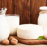 Jug and bottles of milk with a round of cheese, eggs and walnuts on a wooden table