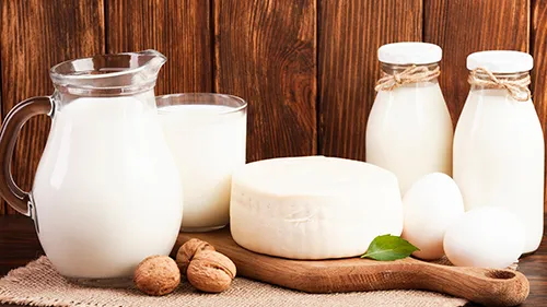 Jug and bottles of milk with a round of cheese, eggs and walnuts on a wooden table