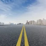Empty asphalt highway with yellow centre lines leading toward a city skyline