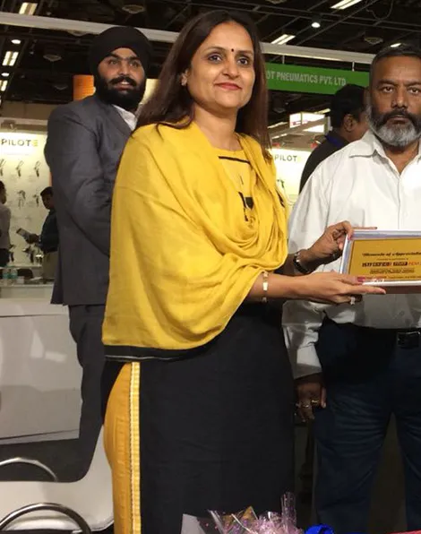 Woman in a yellow scarf holding an award plaque at a trade exhibition