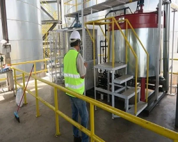 Worker in a hard hat and safety vest beside a bitumen tank with access steps