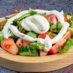 Tomato and cucumber salad drizzled with mayonnaise on a wooden plate with lemon slices