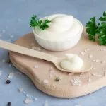 Bowl of mayonnaise with parsley and a wooden spoon on a serving board