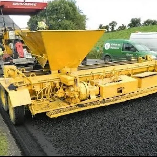 Yellow road surfacing machine with hopper on freshly laid asphalt