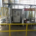 Control panel between two emulsion mixing tanks with yellow access platforms at a jute batching plant