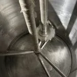 Inside a twin shaft disperser tank showing a saw-tooth dispersion blade and anchor agitator