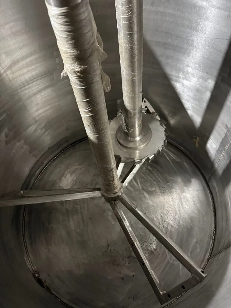 Inside a twin shaft disperser tank showing a saw-tooth dispersion blade and anchor agitator