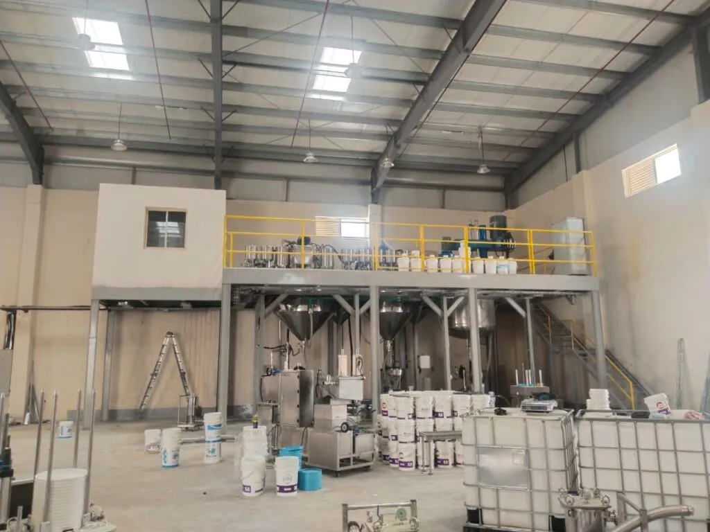 Paint plant with a yellow-railed mezzanine, conical process vessels, paint buckets and IBC totes