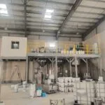 Paint plant with a yellow-railed mezzanine, conical process vessels, paint buckets and IBC totes